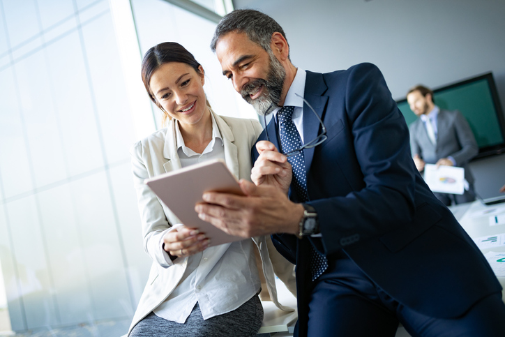 Happy business colleagues in modern office talking and using tablet